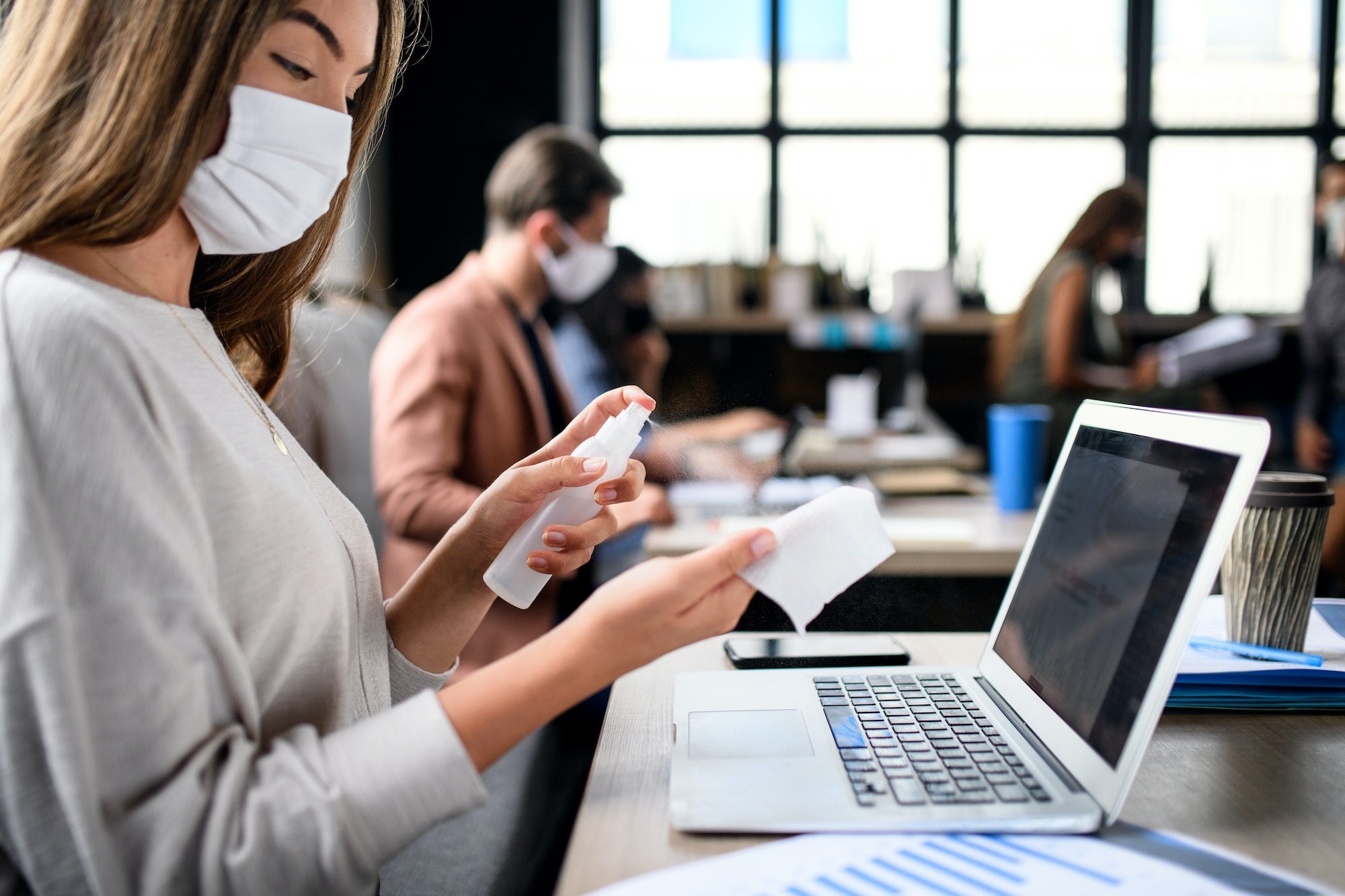 People with face masks disinfecting indoors in office, back to work after coronavirus lockdown